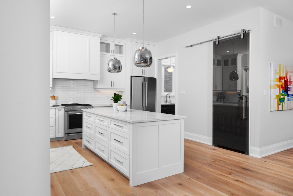 Transitional l-shaped light wood floor and brown floor eat-in kitchen photo in Toronto with an undermount sink, shaker cabinets, white cabinets, marble countertops, white backsplash, subway tile backsplash, stainless steel appliances, an island and white countertops