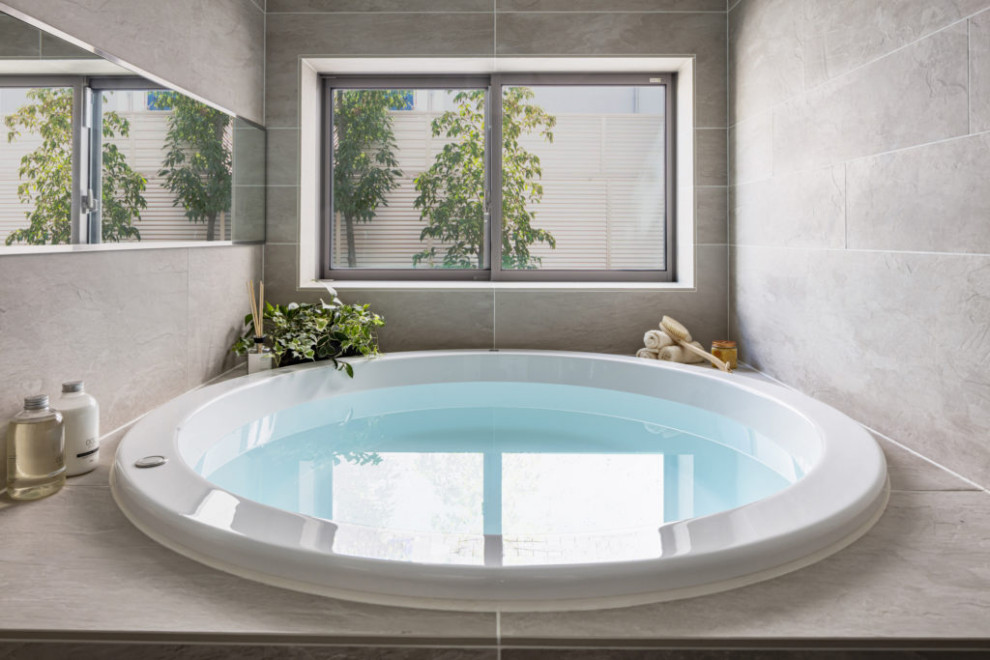 Example of a minimalist beige tile gray floor and tray ceiling drop-in bathtub design in Tokyo with beige walls