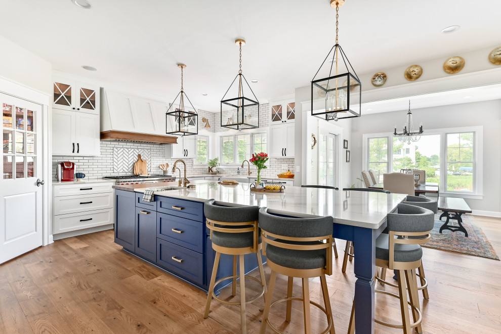 Expansive transitional u-shaped eat-in kitchen in Milwaukee with a farmhouse sink, shaker cabinets, blue cabinets, quartzite benchtops, white splashback, subway tile splashback, stainless steel appliances, vinyl floors, with island, brown floor and white benchtop.