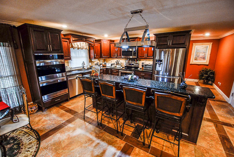 Kitchen - traditional kitchen idea with an undermount sink, raised-panel cabinets, dark wood cabinets, granite countertops, beige backsplash, stone tile backsplash, stainless steel appliances and an island