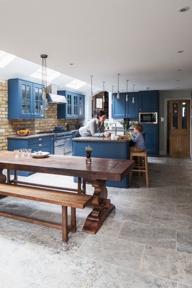 Design ideas for a mid-sized transitional l-shaped eat-in kitchen in London with recessed-panel cabinets, blue cabinets, granite benchtops, beige splashback, brick splashback, stainless steel appliances, with island, grey floor and grey benchtop.