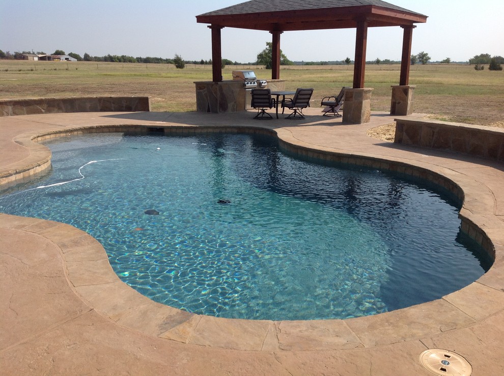 Transitional backyard stamped concrete and custom-shaped pool photo in Dallas