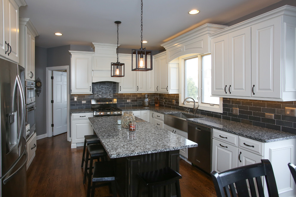 Inspiration for a large transitional u-shaped dark wood floor and brown floor eat-in kitchen remodel in Chicago with white cabinets, gray backsplash, stainless steel appliances, an island, a farmhouse sink, raised-panel cabinets, granite countertops and subway tile backsplash