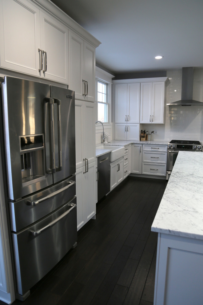 Large transitional l-shaped dark wood floor eat-in kitchen photo in Chicago with recessed-panel cabinets, stainless steel appliances, an island, a farmhouse sink, white cabinets, quartz countertops, white backsplash and subway tile backsplash