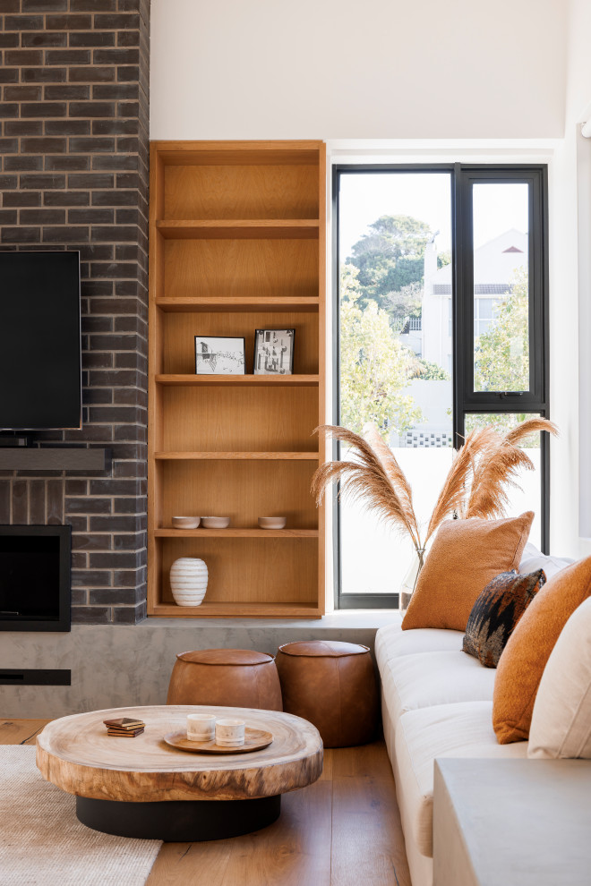 Photo of a mid-sized modern open concept living room in Orange County with medium hardwood floors, a standard fireplace, a brick fireplace surround, a wall-mounted tv, beige floor, vaulted and brick walls.