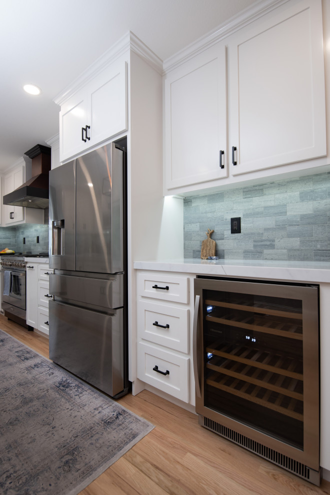 Photo of a modern kitchen/diner in Sacramento with a belfast sink, shaker cabinets, white cabinets, engineered stone countertops, grey splashback, ceramic splashback, stainless steel appliances, an island and white worktops.