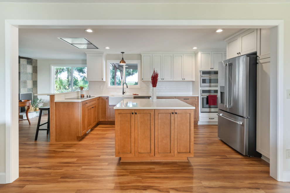Mid-sized transitional l-shaped medium tone wood floor and brown floor eat-in kitchen photo with a farmhouse sink, shaker cabinets, white cabinets, quartz countertops, white backsplash, subway tile backsplash, stainless steel appliances, an island and white countertops