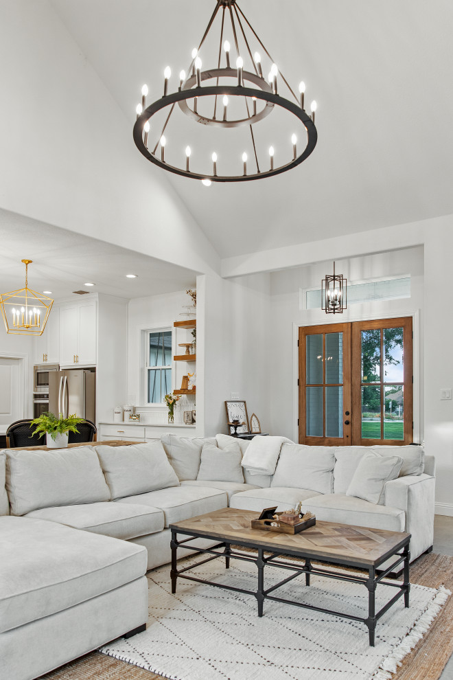 Design ideas for a mid-sized country open concept living room in Dallas with white walls, concrete floors, a standard fireplace, a brick fireplace surround, a wall-mounted tv, beige floor and exposed beam.