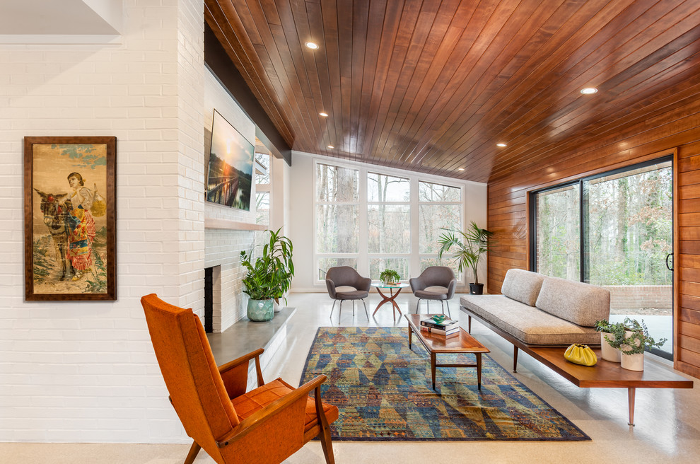 This is an example of a mid-sized midcentury open concept family room in Other with white walls, a brick fireplace surround, a wall-mounted tv and grey floor.