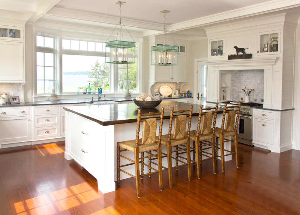 Photo of an expansive beach style u-shaped eat-in kitchen in New York with white cabinets, wood benchtops, grey splashback, medium hardwood floors and with island.