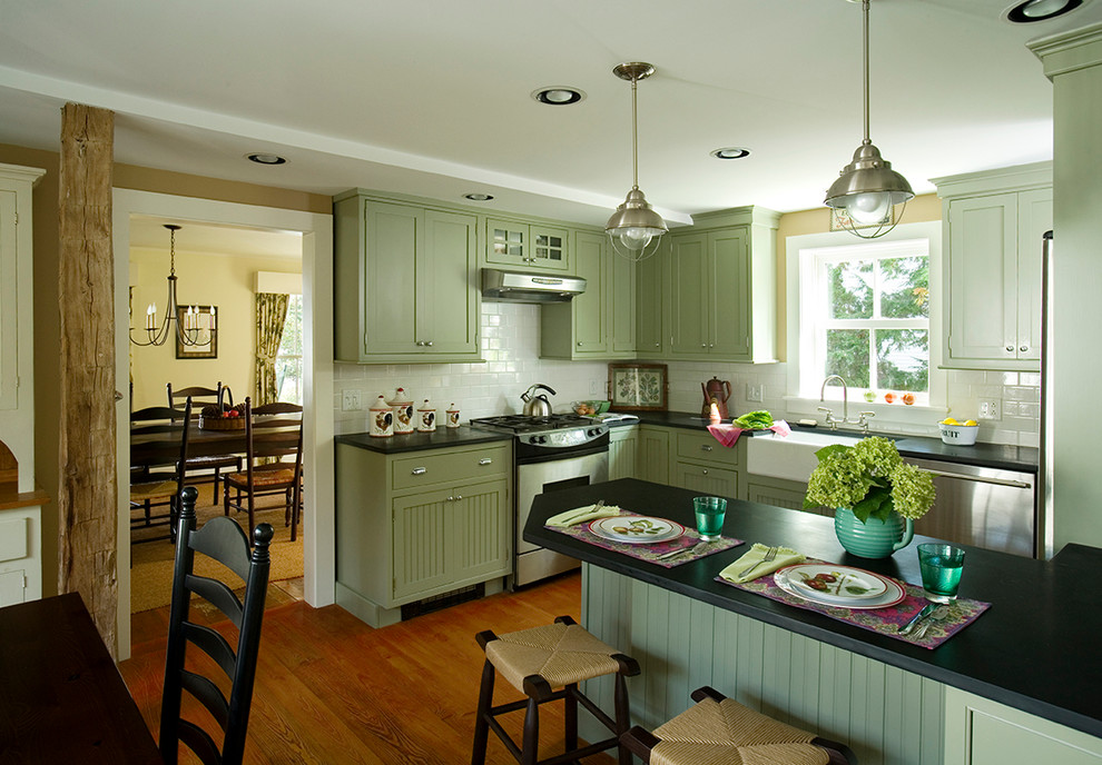 Design ideas for a mid-sized traditional u-shaped eat-in kitchen in Jacksonville with a farmhouse sink, recessed-panel cabinets, green cabinets, soapstone benchtops, white splashback, ceramic splashback, stainless steel appliances, medium hardwood floors and black benchtop.