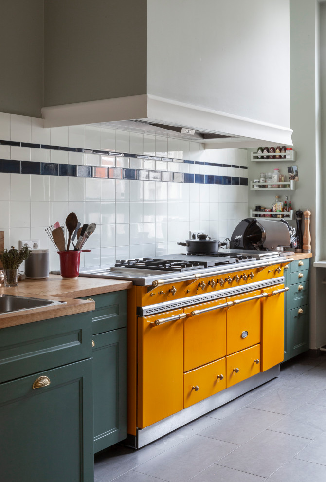 Photo of a mid-sized mediterranean single-wall kitchen in Berlin with a drop-in sink, recessed-panel cabinets, green cabinets, wood benchtops, grey floor and brown benchtop.