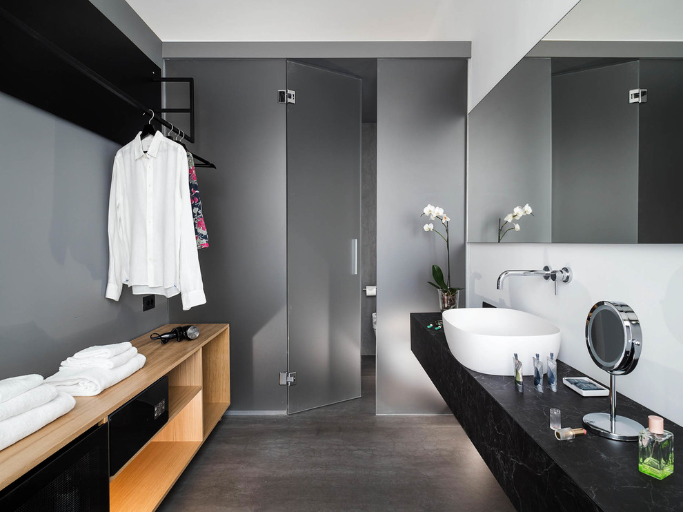 Photo of a contemporary bathroom in Other with black cabinets, a vessel sink, black benchtops, grey walls, grey floor and an enclosed toilet.