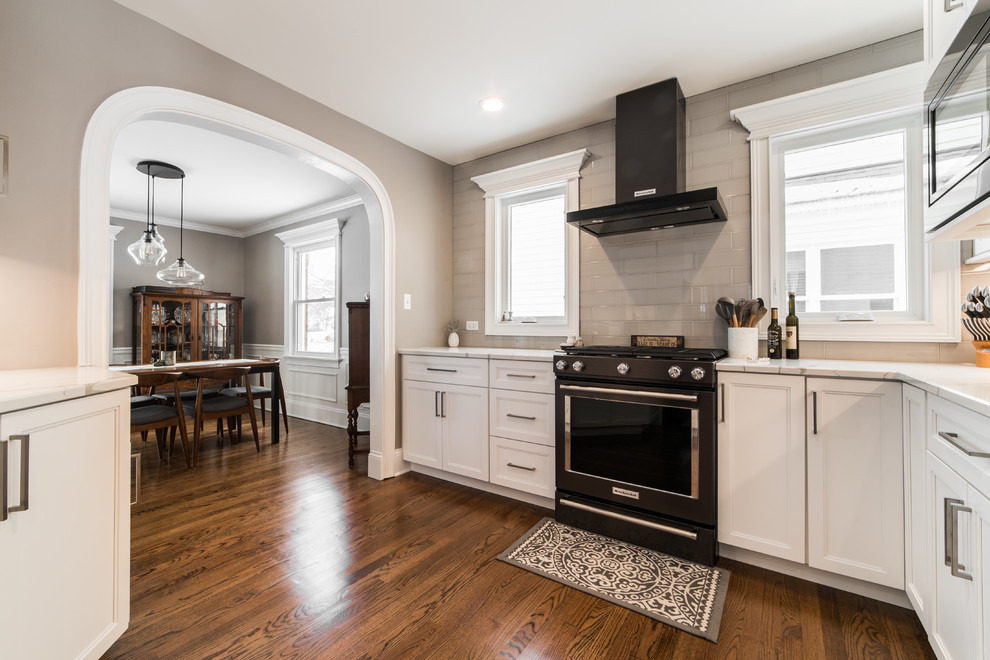 Example of a mid-sized transitional l-shaped medium tone wood floor and brown floor eat-in kitchen design in Chicago with an undermount sink, recessed-panel cabinets, white cabinets, quartzite countertops, gray backsplash, subway tile backsplash, black appliances, no island and multicolored countertops