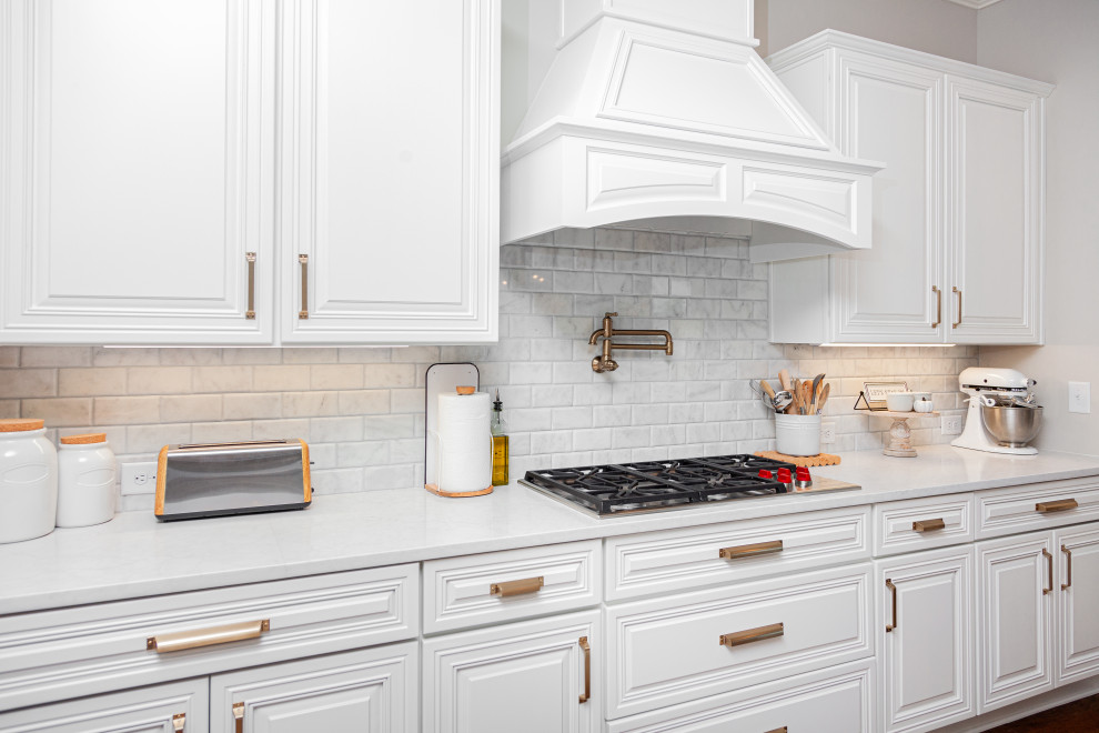 Inredning av ett modernt stort vit vitt kök och matrum, med en enkel diskho, luckor med upphöjd panel, vita skåp, bänkskiva i kvarts, grått stänkskydd, stänkskydd i marmor, rostfria vitvaror, mellanmörkt trägolv, en köksö och brunt golv