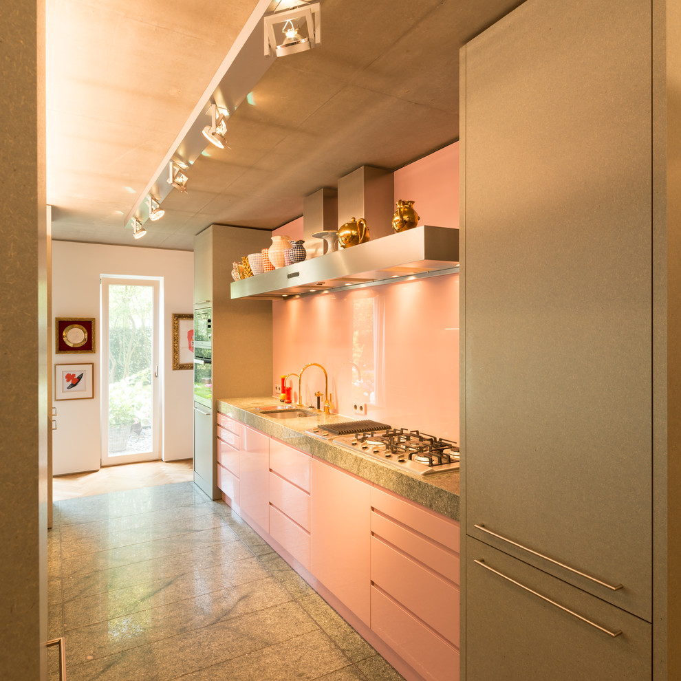 Mid-sized midcentury galley open plan kitchen in Other with a single-bowl sink, flat-panel cabinets, granite benchtops, pink splashback, glass sheet splashback, with island and grey floor.