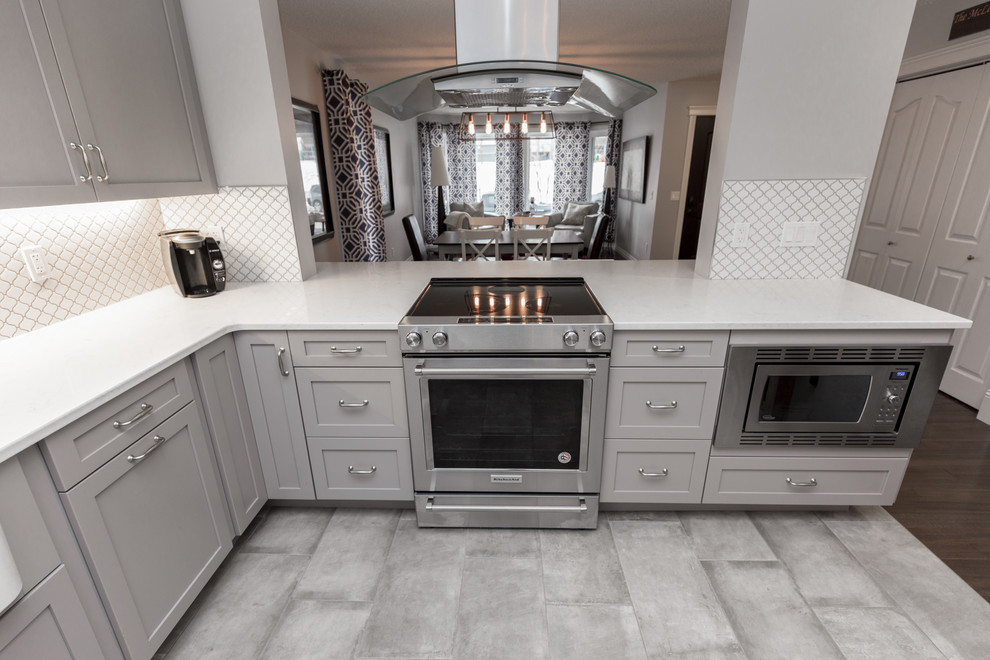 Example of a transitional dark wood floor and brown floor eat-in kitchen design in Calgary with a farmhouse sink, shaker cabinets, gray cabinets, quartz countertops, white backsplash and stainless steel appliances