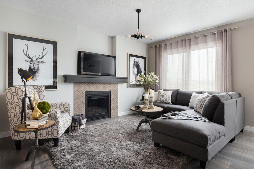 Design ideas for a mid-sized transitional open concept family room in Calgary with beige walls, medium hardwood floors, a standard fireplace, a tile fireplace surround and a freestanding tv.