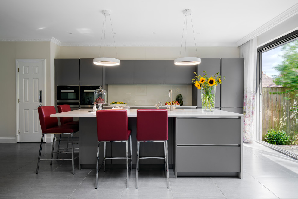 Design ideas for a mid-sized contemporary kitchen in London with flat-panel cabinets, grey cabinets, solid surface benchtops, beige splashback, glass sheet splashback, cement tiles, with island and grey floor.