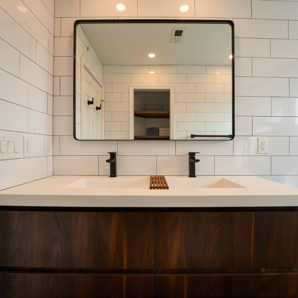 Inspiration for a medium sized modern family bathroom in Philadelphia with flat-panel cabinets, dark wood cabinets, an alcove bath, a shower/bath combination, white tiles, ceramic tiles, white walls, ceramic flooring, an integrated sink, a sliding door, white worktops, double sinks, a two-piece toilet, soapstone worktops, brown floors, an enclosed toilet and a built in vanity unit.