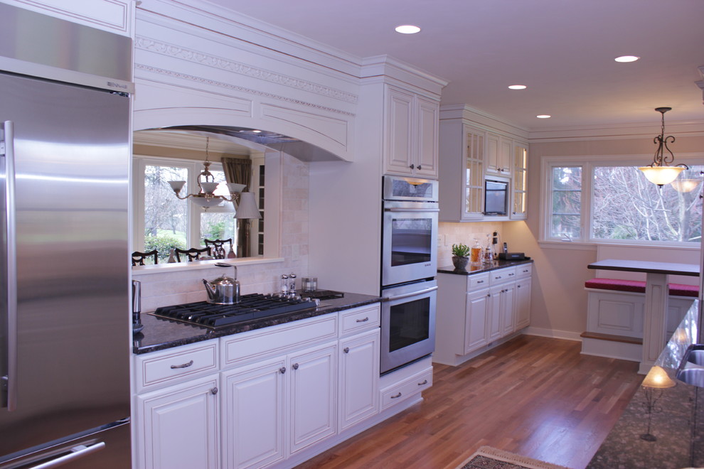 Example of a large transitional galley medium tone wood floor and brown floor eat-in kitchen design with a double-bowl sink, recessed-panel cabinets, white cabinets, granite countertops, beige backsplash, travertine backsplash, stainless steel appliances and no island