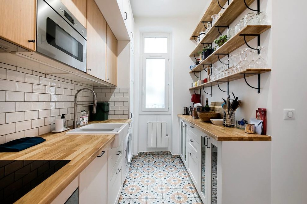 This is an example of a scandinavian galley kitchen in Paris with a farmhouse sink, flat-panel cabinets, light wood cabinets, wood benchtops, white splashback, subway tile splashback and multi-coloured floor.