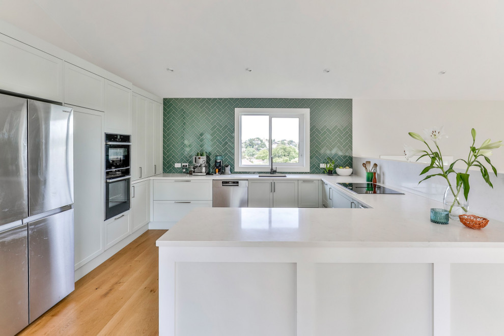 Mid-sized contemporary U-shaped eat-in kitchen in Auckland With an Undermount Sink, Shaker Cabinets, Green Cabinets, Quartz Benchtops, Green Splashback, Subway Tile Splashback, Stainless Steel Appliances, Medium Hardwood Floors, a Peninsula, Brown Floor, White Benchtop and Vaulted.