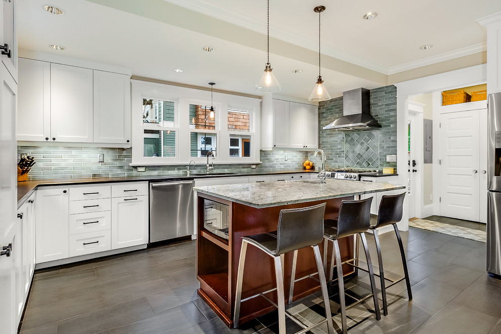 Transitional u-shaped gray floor kitchen photo in Seattle with white cabinets, green backsplash, stainless steel appliances, an island, black countertops, an undermount sink and shaker cabinets