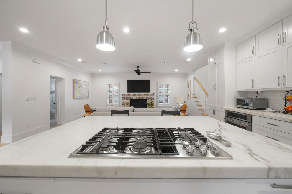 This is an example of a large traditional kitchen in Houston with a belfast sink, shaker cabinets, white cabinets, marble worktops, white splashback, stone tiled splashback, stainless steel appliances, light hardwood flooring, an island and yellow worktops.