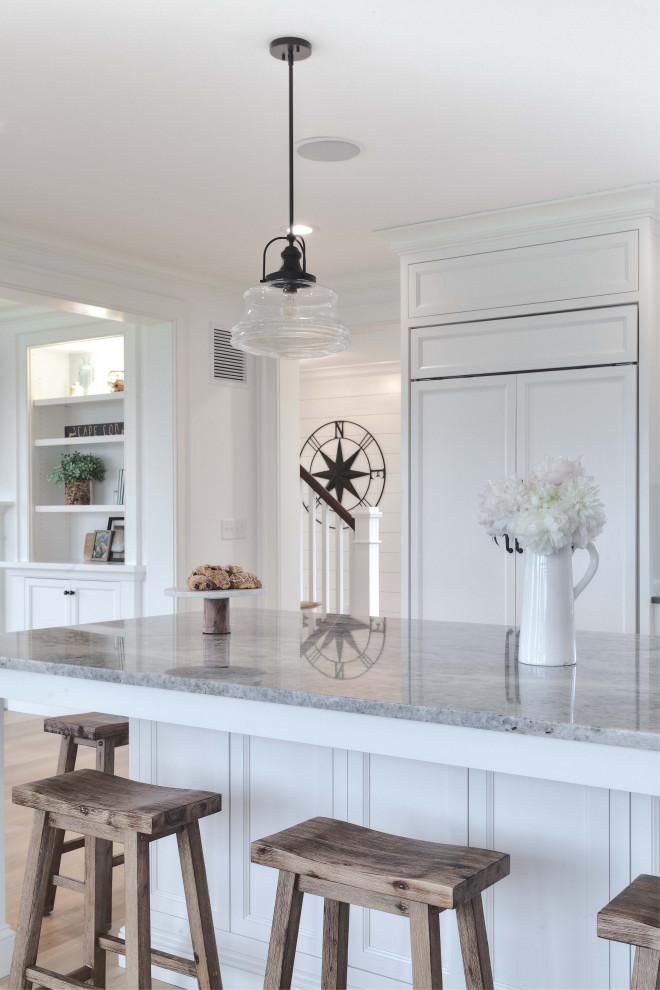 Cette image montre une cuisine américaine marine avec des portes de placard blanches, un plan de travail en quartz, parquet clair, îlot, un plan de travail gris et un placard à porte affleurante.