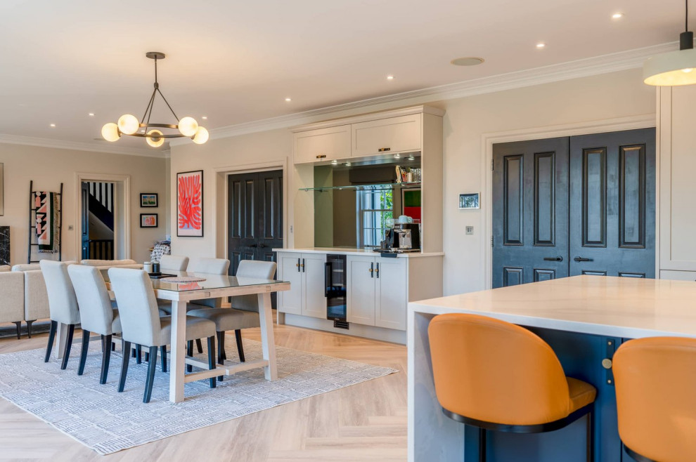 This is an example of a large classic single-wall open plan kitchen in Hertfordshire with a single-bowl sink, recessed-panel cabinets, grey cabinets, quartz worktops, black appliances, light hardwood flooring, an island, brown floors and white worktops.