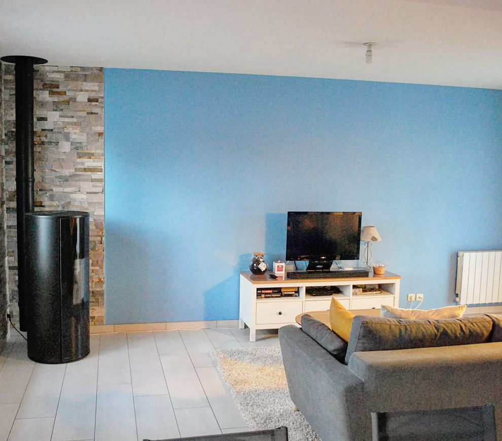 Foto di un soggiorno eclettico di medie dimensioni e aperto con pareti blu, pavimento con piastrelle in ceramica, stufa a legna, cornice del camino in pietra ricostruita, TV autoportante e pavimento bianco