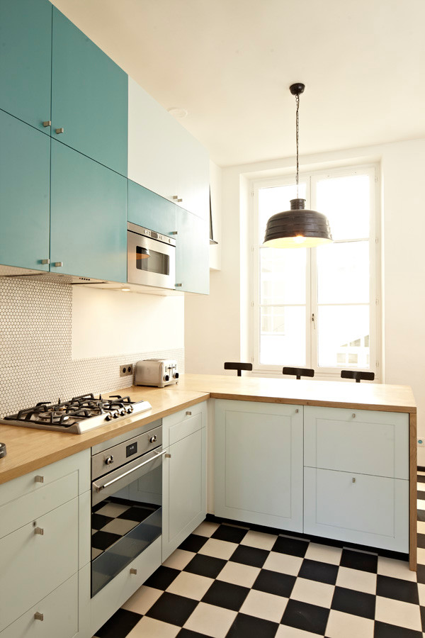 This is an example of a large eclectic kitchen in Paris with blue cabinets, wood benchtops, blue splashback, timber splashback, stainless steel appliances, cement tiles and multi-coloured floor.