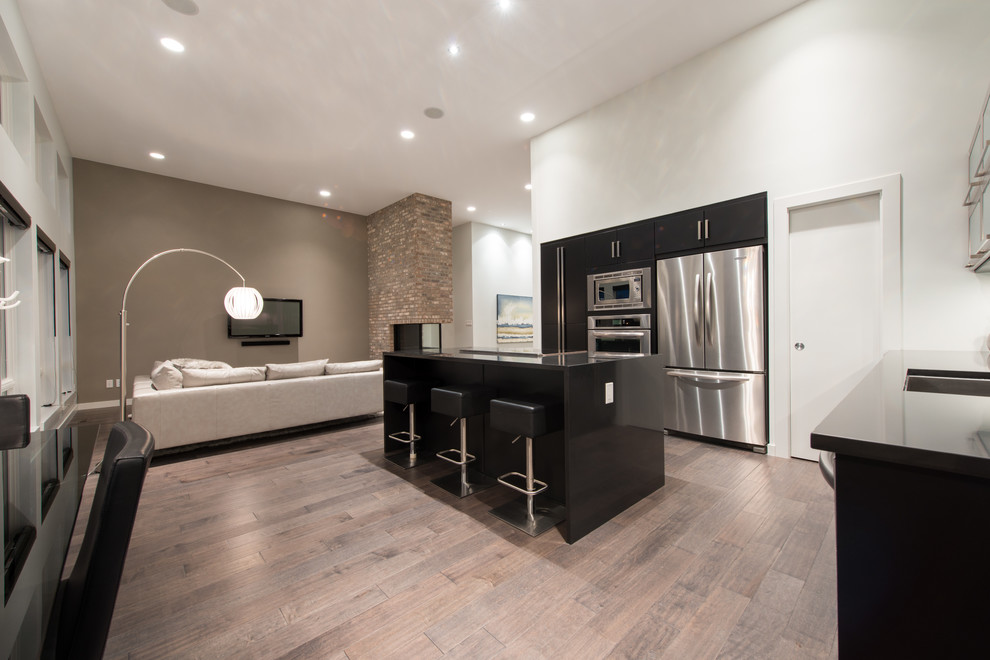 Large contemporary l-shaped open plan kitchen in Other with a single-bowl sink, flat-panel cabinets, black cabinets, quartzite benchtops, glass sheet splashback, stainless steel appliances, dark hardwood floors, with island, brown floor and black benchtop.