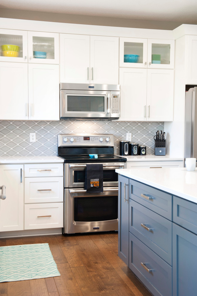 Inspiration for a mid-sized transitional l-shaped medium tone wood floor and brown floor eat-in kitchen remodel with an undermount sink, shaker cabinets, white cabinets, quartz countertops, gray backsplash, mosaic tile backsplash, stainless steel appliances, an island and white countertops