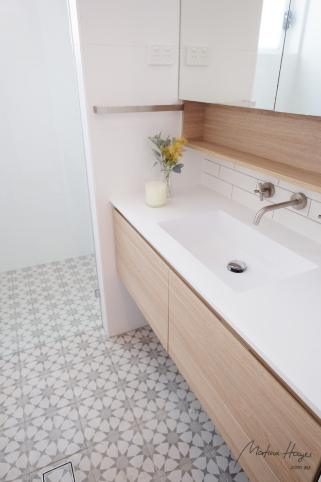 Photo of a medium sized contemporary ensuite bathroom in Sydney with flat-panel cabinets, light wood cabinets, a built-in shower, a one-piece toilet, white tiles, ceramic tiles, white walls, porcelain flooring, a built-in sink, engineered stone worktops, grey floors, an open shower, white worktops, a laundry area, a single sink and a built in vanity unit.