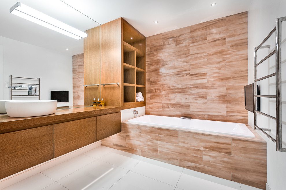 Contemporary bathroom in Auckland with a vessel sink, a drop-in tub, flat-panel cabinets, medium wood cabinets, wood benchtops, multi-coloured tile and porcelain tile.