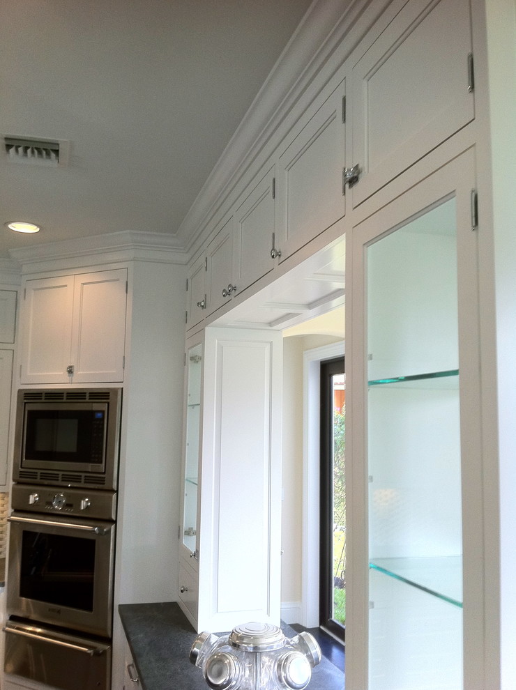 Example of a large transitional u-shaped dark wood floor and brown floor open concept kitchen design in Miami with a farmhouse sink, shaker cabinets, white cabinets, granite countertops, multicolored backsplash, stone tile backsplash, stainless steel appliances and an island