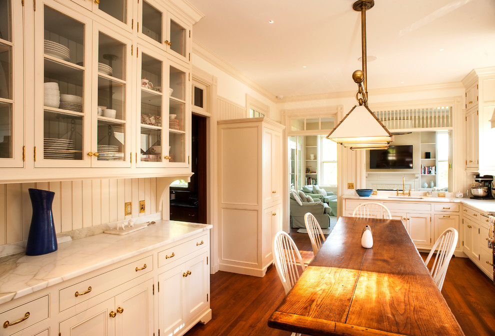 Photo of a mid-sized traditional galley eat-in kitchen in Portland Maine with an undermount sink, recessed-panel cabinets, white cabinets, marble benchtops, white splashback, porcelain splashback, black appliances, medium hardwood floors, no island and brown floor.
