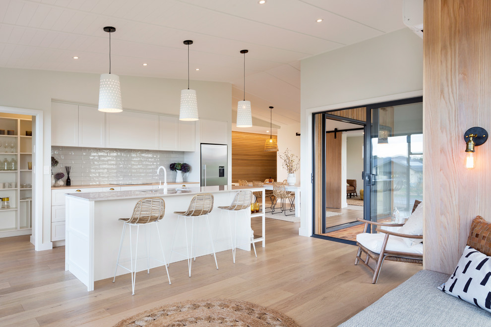 Design ideas for a mid-sized scandinavian galley eat-in kitchen in Auckland with white splashback, subway tile splashback, light hardwood floors, with island, an undermount sink, shaker cabinets, white cabinets, quartz benchtops and stainless steel appliances.