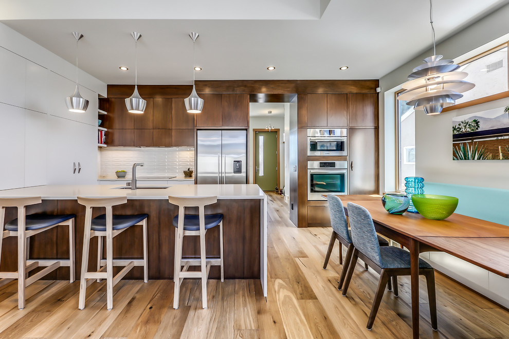 Inspiration for a mid-sized contemporary u-shaped eat-in kitchen in Calgary with a single-bowl sink, flat-panel cabinets, quartz benchtops, white splashback, ceramic splashback, stainless steel appliances, medium hardwood floors, a peninsula, dark wood cabinets and brown floor.