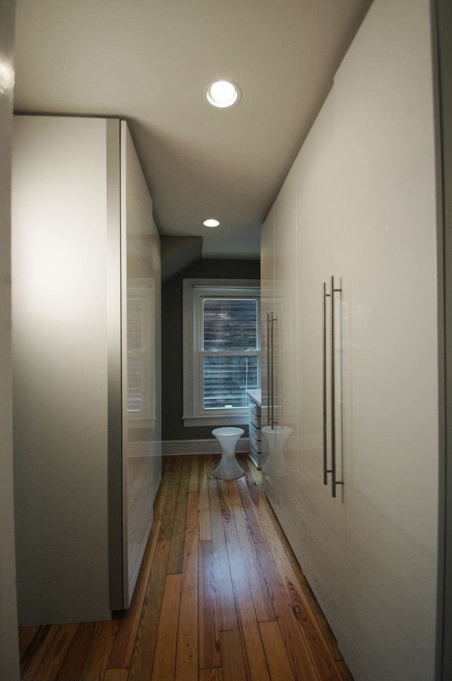 Mid-sized contemporary gender-neutral dressing room in DC Metro with flat-panel cabinets, white cabinets and light hardwood floors.