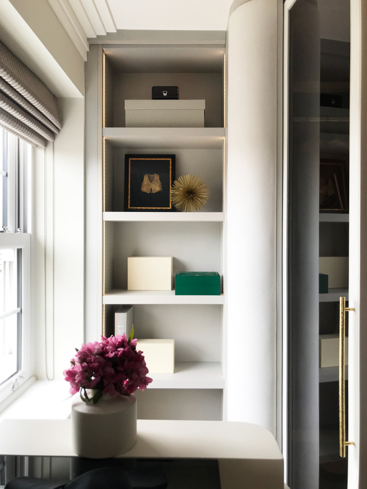 Medium sized contemporary gender neutral built-in wardrobe in London with glass-front cabinets, light wood cabinets, carpet, beige floors and feature lighting.