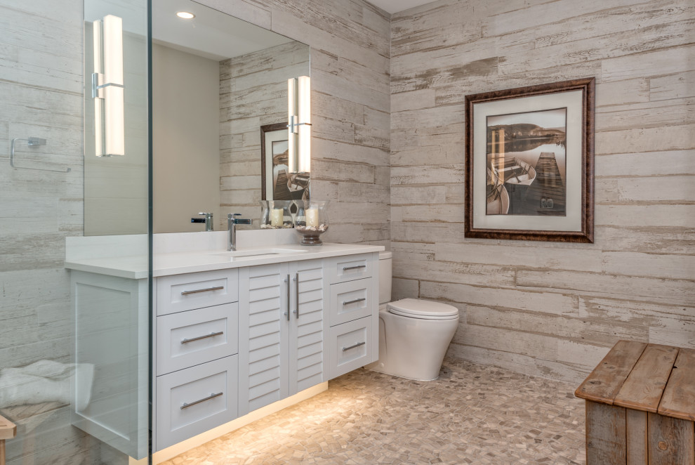 Photo of a beach style bathroom in Vancouver with louvered cabinets, white cabinets, beige tile, pebble tile floors, an undermount sink, beige floor and white benchtops.