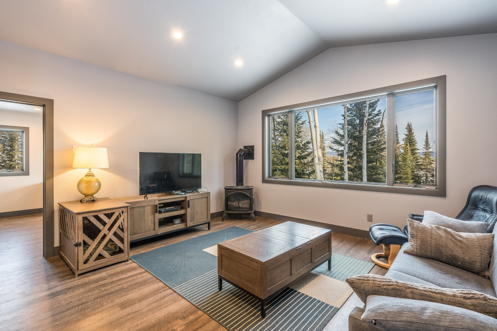 Abgetrenntes Rustikales Wohnzimmer mit beiger Wandfarbe, Vinylboden, Kaminofen, freistehendem TV, beigem Boden und gewölbter Decke in Denver
