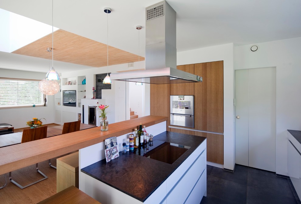 Mid-sized contemporary u-shaped open plan kitchen in Munich with flat-panel cabinets, stainless steel appliances, slate floors, a peninsula, black floor and black benchtop.