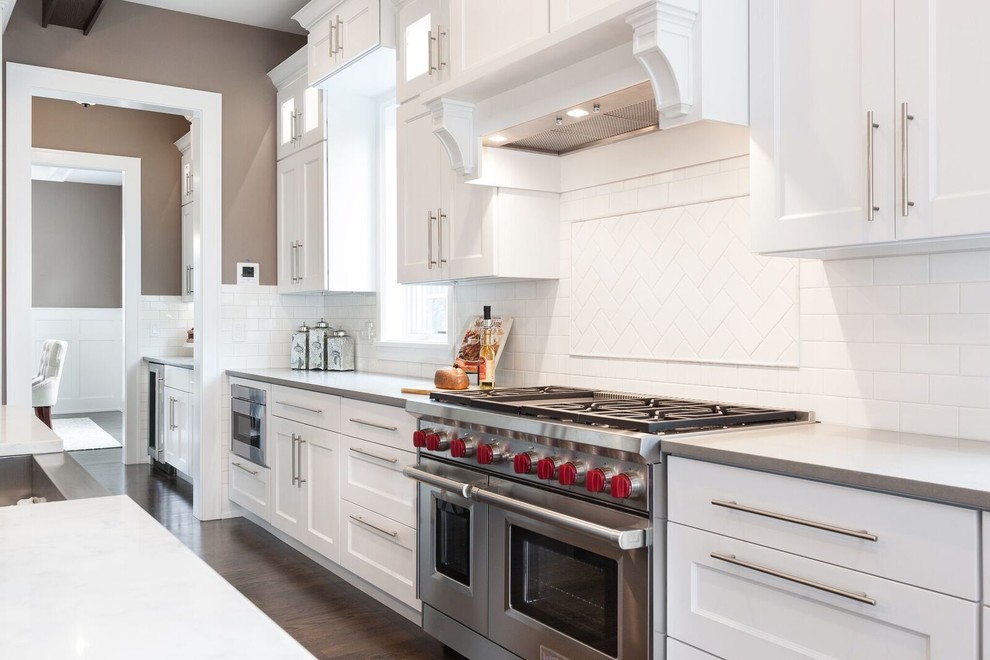 Transitional u-shaped dark wood floor open concept kitchen photo in Chicago with a farmhouse sink, shaker cabinets, white cabinets, quartz countertops, white backsplash, subway tile backsplash, stainless steel appliances, an island and white countertops