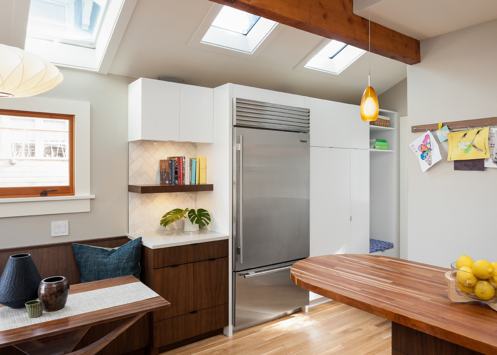 Inspiration for a mid-sized 1960s l-shaped medium tone wood floor eat-in kitchen remodel in Seattle with an undermount sink, flat-panel cabinets, medium tone wood cabinets, quartz countertops, white backsplash, stone tile backsplash, stainless steel appliances and a peninsula