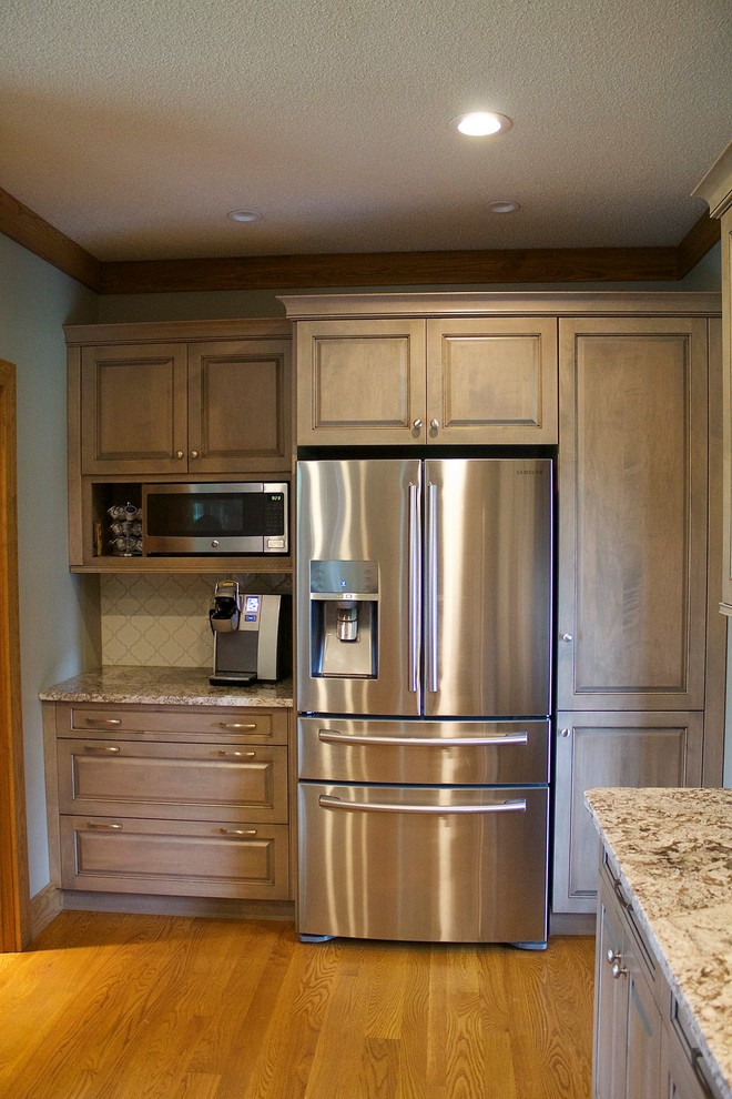 Mid-sized transitional galley medium tone wood floor eat-in kitchen photo with a farmhouse sink, recessed-panel cabinets, gray cabinets, granite countertops, white backsplash, ceramic backsplash, stainless steel appliances and a peninsula