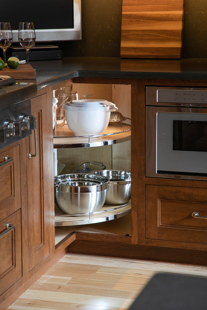 Mid-sized mountain style l-shaped light wood floor open concept kitchen photo in Milwaukee with recessed-panel cabinets, medium tone wood cabinets, quartz countertops, gray backsplash, stone slab backsplash, stainless steel appliances, gray countertops and an island